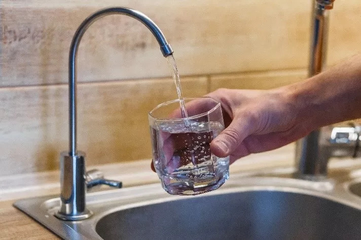 Рука наливает фильтрованную питьевую воду из крана в стакан.